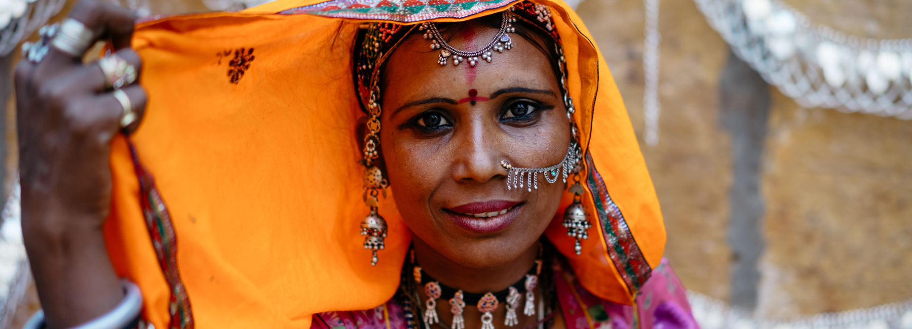 A smiling woman wearing elaborate facial jewellery an orange and pink scarf over her head